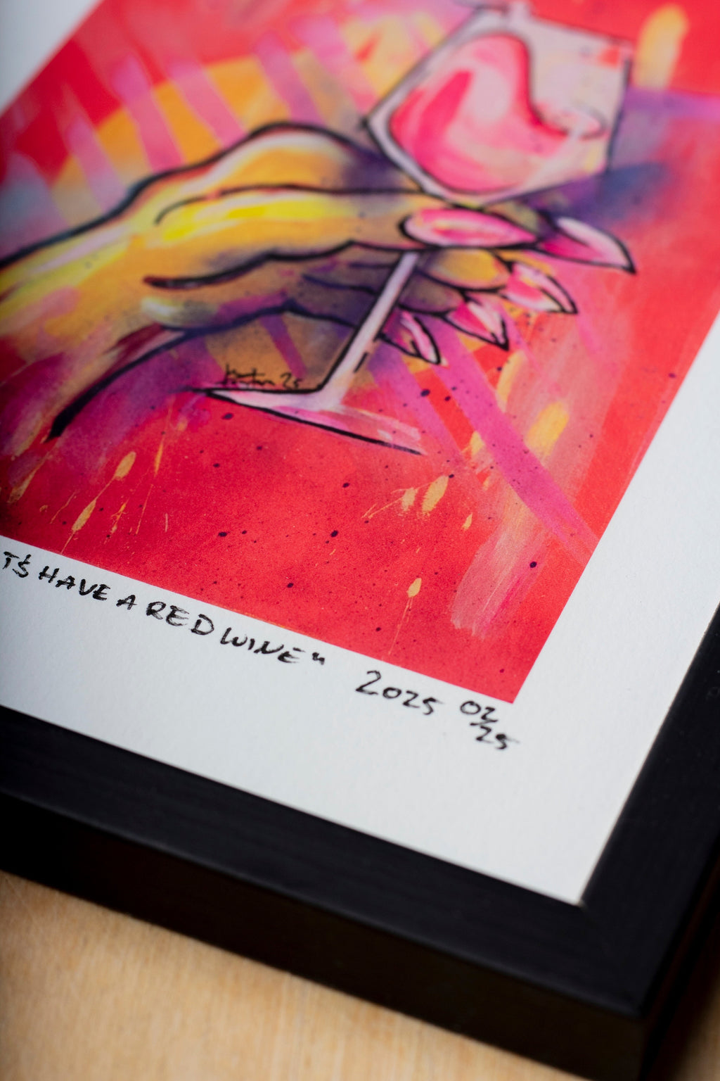 Zeitgenössischer gerahmter Kunstdruck eines figurativen Gemäldes mit stilisierter Hand und Weinglas in intensiven Neonfarben. Detailreiche Darstellung in Pink-, Gelb- und Orangetönen auf leuchtendem Hintergrund, präsentiert als signierter Print mit Passepartout in schwarzem Rahmen auf Holzoberfläche. Bildausschnitt mit Fokus auf Jahr und Limitierung.