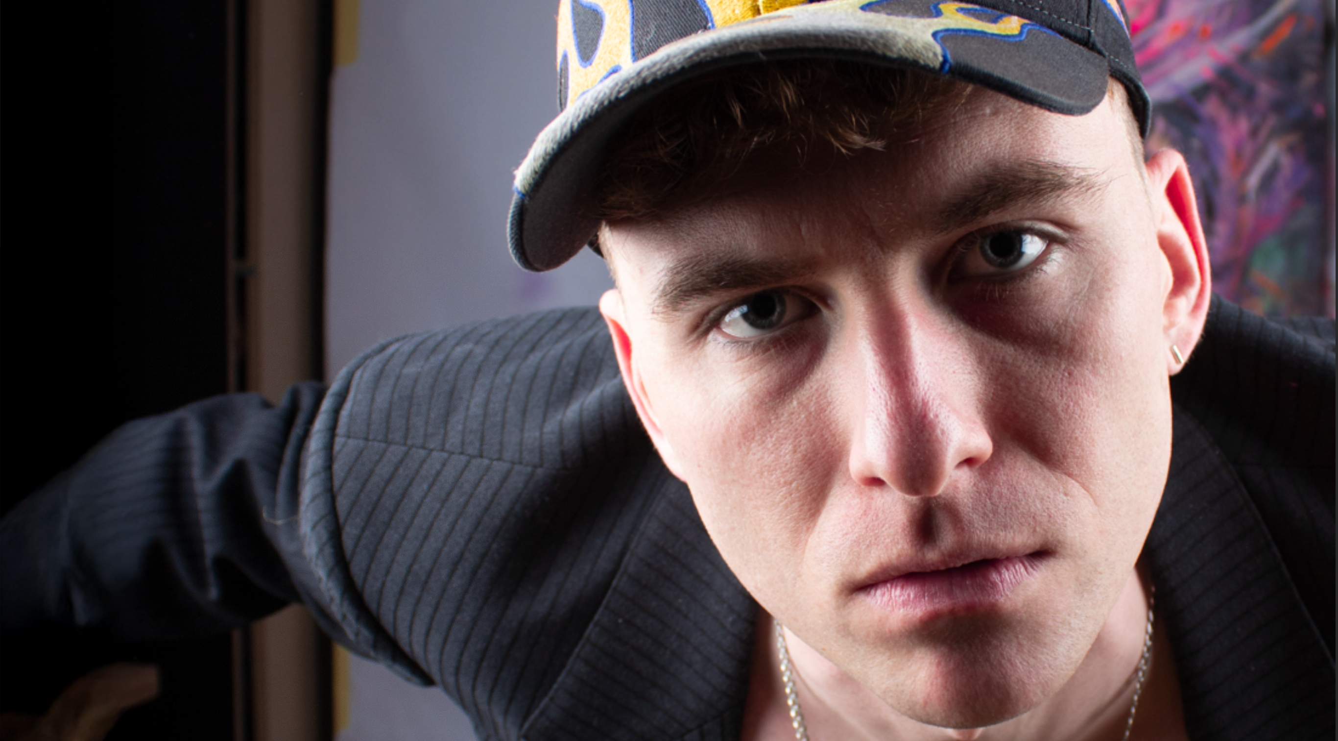 Nahaufnahme eines zeitgenössischen Künstlers mit Cap mit Flammendekor und direktem, fokussierten Blick in die Kamera im Atelier 